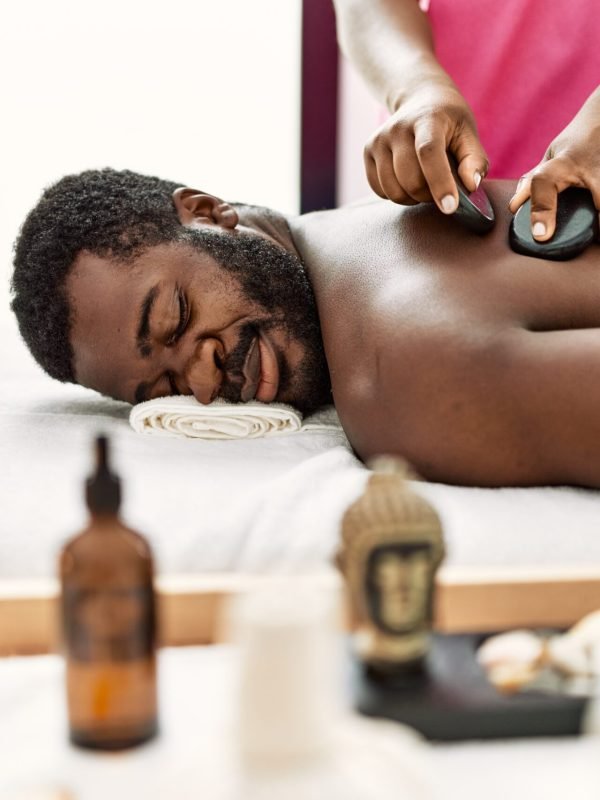 African american man reciving back massage with black stones at beauty center.