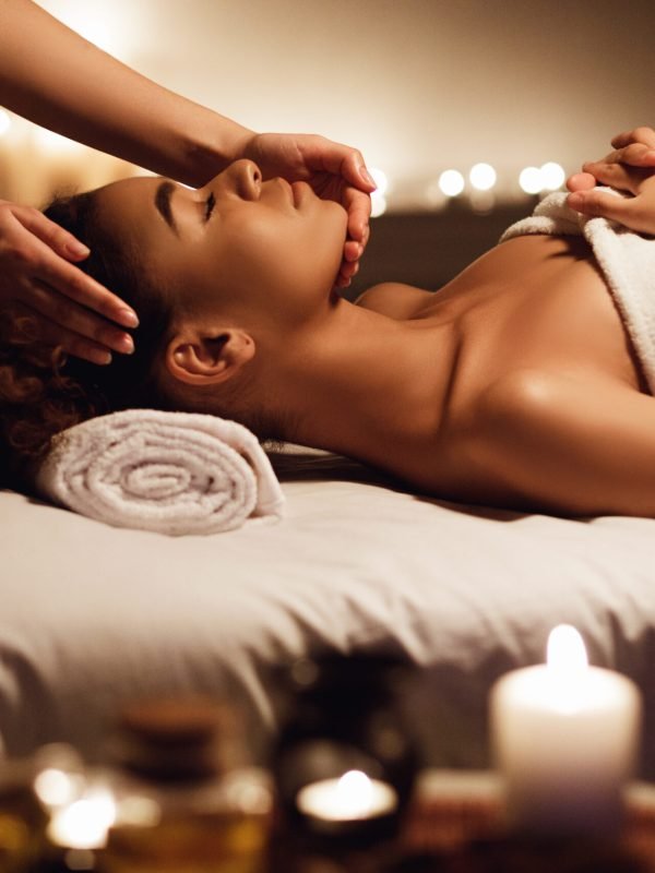 African girl having face massage, relaxing in spa salon, side view