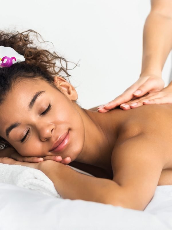African-american girl enjoying back massage in spa salon, relaxing with closed eyes